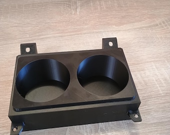 Könnte beinhalten: Ein schwarzer, rechteckiger Getränkehalter mit zwei kreisförmigen Öffnungen. Der Halter hat einen erhöhten Rand und Befestigungslaschen. Er besteht aus mattschwarzem Material und liegt auf einer hellen Holzoberfläche. Maße: ca. 15 cm x 8 cm.