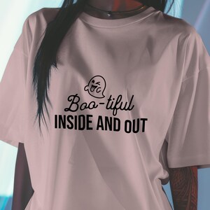 Puede incluir: Una camiseta rosa claro con un gráfico de fantasma negro y el texto "Boo-tiful Inside and Out".