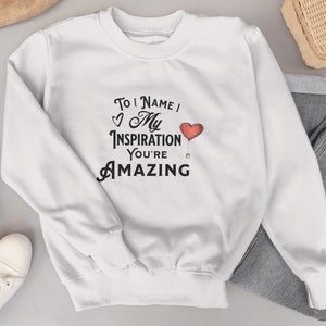 Puede incluir: Sudadera blanca con un gráfico negro que dice "To [Name] My Inspiration You're Amazing" con una ilustración de un globo de corazón rojo.