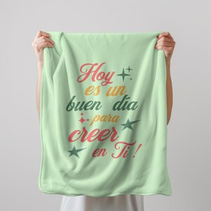 Puede incluir: Una manta de forro polar verde claro con el texto "Hoy es un buen dia para creer en Ti!" en letras de colores con estrellas.