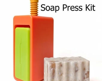 May include: A bright orange and green soap press kit with the text "Soap Press Kit". The kit includes a rectangular press and a bar of soap. The press has a yellow handle and a green insert.