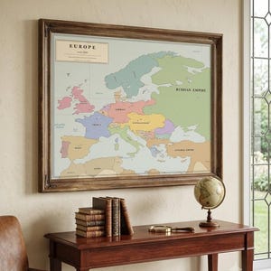 Może przedstawiać: Oprawiona historyczna mapa Europy z około 1900 roku w stonowanych pastelowych kolorach, przedstawiająca oznaczone regiony, takie jak Imperium Rosyjskie, Niemcy, Francja i Imperium Osmańskie, w ciemnej drewnianej ramie z ozdobnymi rzeźbieniami.