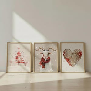 May include: Three framed watercolor prints. One features a red Christmas tree with a star, another a goat wearing a red scarf, and the last a woven heart. All are set against a neutral background.