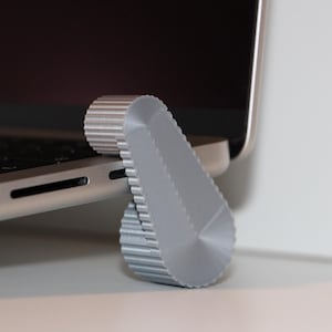 Könnte beinhalten: Ein grauer Laptopständer aus Kunststoff mit einer strukturierten Oberfläche. Der Ständer ist so konzipiert, dass er einen Laptop für eine bessere Ergonomie anhebt.