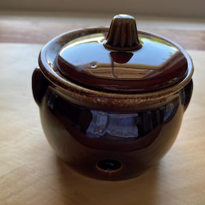 May include: A brown ceramic pot with a lid. The pot has a round body and a small knob on the lid.