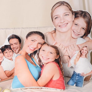 May include: A collection of custom-shaped pillows featuring family portraits. The pillows depict smiling faces of adults and children. The pillows are in various sizes and shapes, with vibrant colors and realistic details.