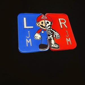 May include: A split design featuring a cartoon character, half in color and half as a skeleton. The left side is blue with the letter "L" and the letters "J" and "M". The right side is red with the letter "R" and the letters "J" and "M".