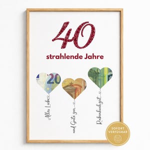 Op de afbeelding: Een ingelijste print met het grote rode getal 40 en de tekst strahlende Jahre. Daaronder staan drie hartvormige uitsnedes gemaakt van eurobiljetten, elk met een dunne lijn en de tekst Alles Liebe, und Gute zur, en Rubinhochzeit.