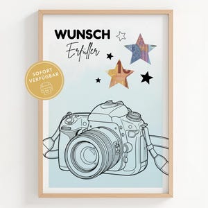 May include: A framed art print with a line drawing of a camera. The print includes the words "Wunsch Erfüller" and star graphics. A gold sticker with the words "SOFORT VERFÜGBAR" is in the lower left corner.