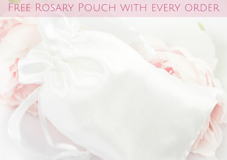 May include: A white satin rosary pouch with a drawstring closure, set against a backdrop of soft pink and white flowers. The text "FREE ROSARY POUCH WITH EVERY ORDER" is displayed at the top.