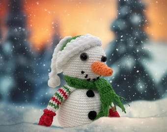 May include: A white crocheted snowman with a green scarf and red mittens, wearing a white and green hat. The snowman is standing in a snowy landscape with a blurred background of trees and a sunset.