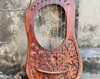 Könnte beinhalten: Eine hölzerne Leier mit einem floralen Design, das in den Korpus geschnitzt ist. Die Leier hat 10 Saiten und einen Steg aus Holz.