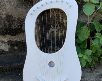 May include: A white lyre harp with a rounded body and a large central sound hole. The harp has 10 strings and a curved bridge. The instrument is made of wood and has a smooth, painted finish. The lyre is a stringed musical instrument.