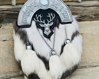 May include: A white and brown fur sporran with a silver stag head and Celtic knot design on the flap. The sporran has three white fur tassels.