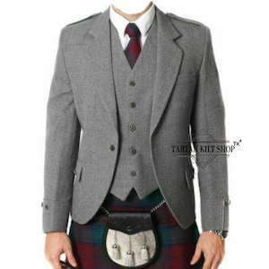 May include: A grey tweed jacket, waistcoat, and tie ensemble. The jacket features a two-button fastening and notched lapels. The waistcoat has a five-button closure. The tie is red and navy. The outfit is worn with a tartan kilt and sporran.