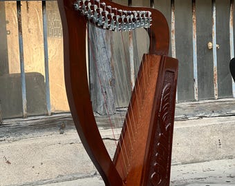 May include: A mahogany-colored harp with silver tuning pegs and strings. The wooden body features carved decorative elements. The harp is positioned against a weathered, textured background, suggesting an antique or vintage aesthetic.