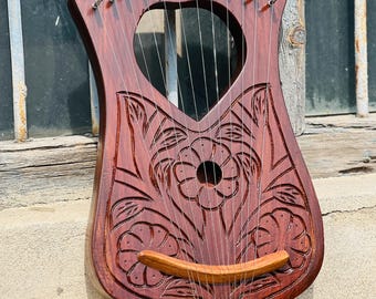 Puede incluir: Un laúd de madera con un diseño floral tallado en el cuerpo. El laúd tiene 10 cuerdas y un puente de madera.