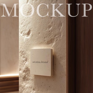 May include: A white square sign with the text "aroma.brand" on a textured beige wall. The sign is mounted on the wall with a small gap between the sign and the wall.