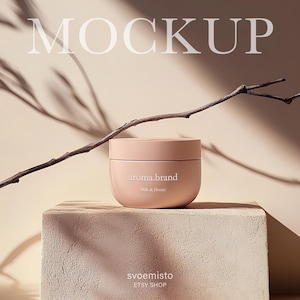 Puede incluir: Un tarro de crema corporal rosa claro con el texto "aroma.brand Milk & Honey" en la parte delantera. El tarro está colocado sobre una plataforma de madera marrón claro con una rama de ramitas en la parte superior. El fondo es de color beige claro.