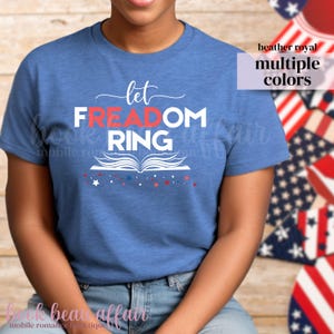 May include: Heather royal blue t-shirt with the words "Let Freedom Ring" in white and red, with an open book graphic. The shirt has a crew neck and short sleeves. The words "multiple colors" are also visible.