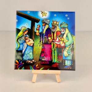 May include: A square ceramic tile featuring a colorful illustration of the Nativity scene. The artwork depicts Mary holding baby Jesus, with the three wise men bearing gifts. The background is a starry night with a wooden structure.