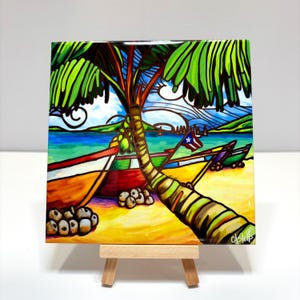 May include: A colorful ceramic tile painting depicting a tropical beach scene with palm trees, boats, and coconuts. The tile is on a small wooden easel.