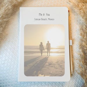 May include: A white notebook featuring a photograph of two people walking along a beach at sunset. The text "Me & You Cancun Beach, Mexico" is printed on the front of the notebook.