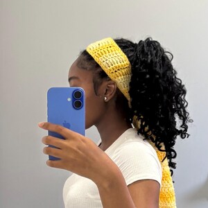May include: A yellow and white crochet headband. The headband is made of a soft, textured yarn and is designed to keep hair out of the face. The headband is a stylish accessory for any outfit. The crochet pattern is visible.