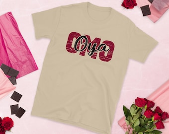 Puede incluir: Una camiseta beige con un gráfico rojo y negro que dice "OMO Oya".