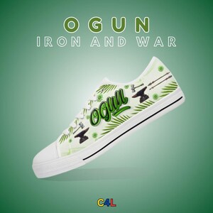 Puede incluir: Zapatillas bajas de lona blancas con un estampado verde y blanco que presenta la palabra "Ogun" en letras verdes cursivas, un yunque, un martillo y flechas. El texto "Iron and War" está impreso en negro sobre el zapato.