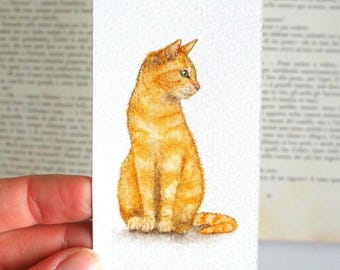 May include: A rectangular bookmark featuring a watercolor illustration of a ginger tabby cat sitting in profile. The cat has orange fur with darker stripes, pointed ears, and green eyes, rendered on a textured white paper background.