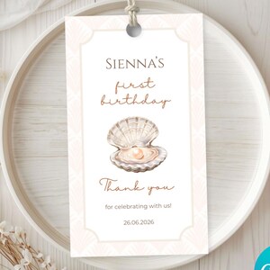 Può includere: Un'etichetta regalo rettangolare bianca con un bordo geometrico rosa chiaro, che presenta il testo Sienna's first birthday, un'illustrazione ad acquerello di una conchiglia aperta con una perla e il testo Thank you for celebrating with us! 26.06.2026.