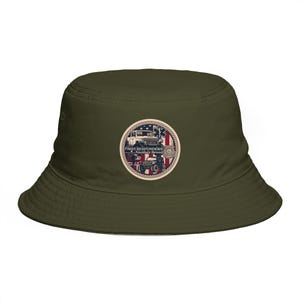 Pode incluir: Chapéu de balde verde-oliva com um emblema circular. O emblema apresenta dois veículos off-road, a bandeira americana e o texto "FIRST RESPONDERS Another Breed". O chapéu tem uma aba larga.