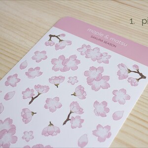 Pode incluir: Uma folha de adesivos rosa com ilustra&ccedil;&otilde;es de flores de cerejeira e p&eacute;talas. A folha &eacute; etiquetada como "maple & matsu" e "sakura season".