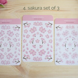 Pode incluir: Tr&ecirc;s folhas de adesivos de flores de cerejeira rosa e branco. Cada folha tem um arranjo diferente de flores e p&eacute;talas. As folhas s&atilde;o etiquetadas como "maple & matsu" e "sakura season".
