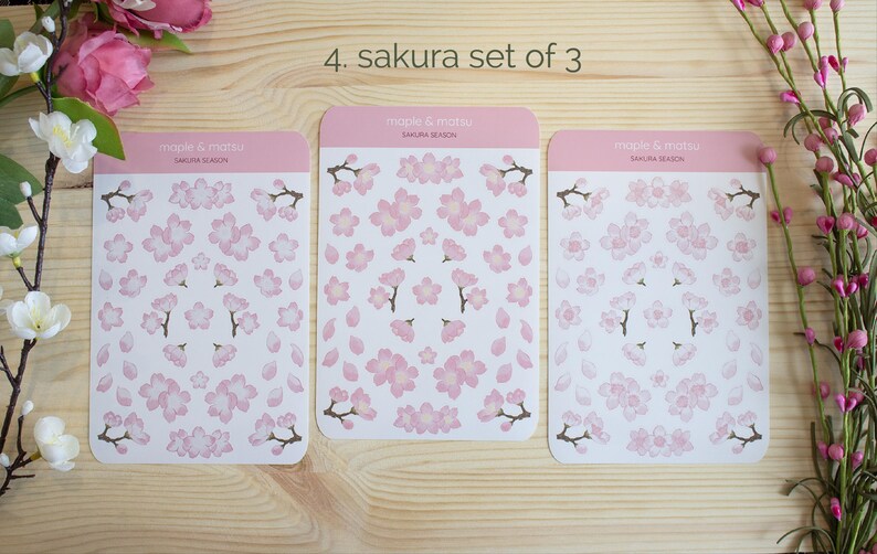 Pode incluir: Tr&ecirc;s folhas de adesivos de flores de cerejeira rosa e branco. Cada folha tem um arranjo diferente de flores e p&eacute;talas. As folhas s&atilde;o etiquetadas como "maple & matsu" e "sakura season".