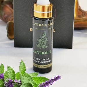 Peut inclure: Une petite bouteille en verre brun foncé avec un bouchon doré et un compte-gouttes blanc. La bouteille est étiquetée "Patchouli Huile Essentielle Qualité Premium 10ml ou 0.33 Fl.Oz".