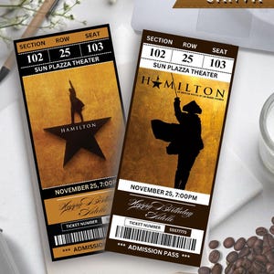 May include: Two tickets for the musical "Hamilton" with gold and brown backgrounds. Each ticket shows section 102, row 25, seat 103 for the Sun Plazza Theater on November 25th. The tickets are labeled "Happy Birthday Adelle".