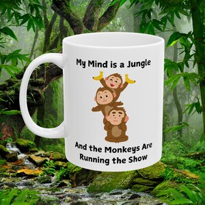 May include: White ceramic mug with a black and brown illustration of three monkeys holding bananas. The text "My Mind is a Jungle and the Monkeys Are Running the Show" is printed on the mug.