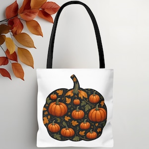 Puede incluir: Bolso tote blanco con asas negras. Presenta un diseño de calabaza grande lleno de calabazas naranjas y hojas de otoño sobre un fondo negro. Ideal para ir de compras o transportar objetos.