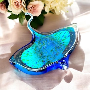 Puede incluir: Una escultura de vidrio azul en forma de manta raya con detalles de purpurina verde y azul.