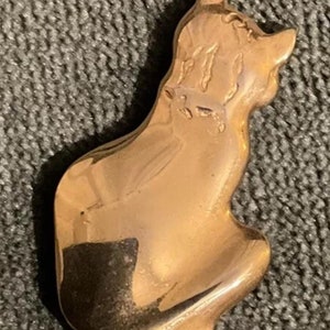 May include: A gold-toned metal brooch in the shape of a sitting cat. The cat's tail is curled around its body.