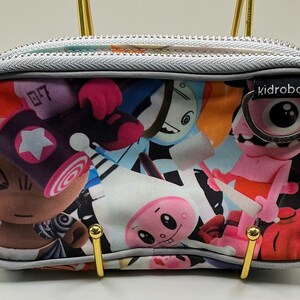 May include: A gray zippered pouch with a colorful graphic print featuring various cartoon characters. The pouch has gold-colored hardware and the "kidrobot" logo. The print includes figures in shades of pink, blue, orange, and brown.