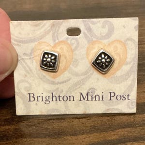 Puede incluir: Un par de pendientes cuadrados de tono plateado con un motivo floral central en una tarjeta de presentación con la etiqueta Brighton Mini Post. Los pendientes tienen un acabado oxidado oscuro dentro del marco cuadrado sobre fondo claro.