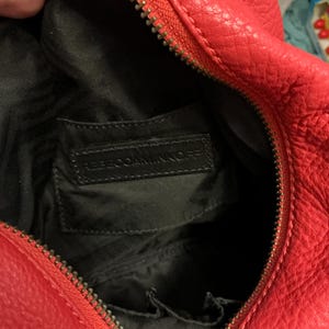 May include: A bright red textured handbag with a gold-toned zipper closure. The interior is lined with black fabric and features a rectangular black leather patch embossed with the text REBECCAMINKOFF, along with small internal pockets.