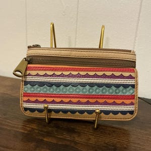 May include: A colourful leather wallet with a zip closure. The wallet has a decorative pattern of horizontal stripes in various colours, including red, orange, blue, and purple. The zip pull and hardware are gold-toned.