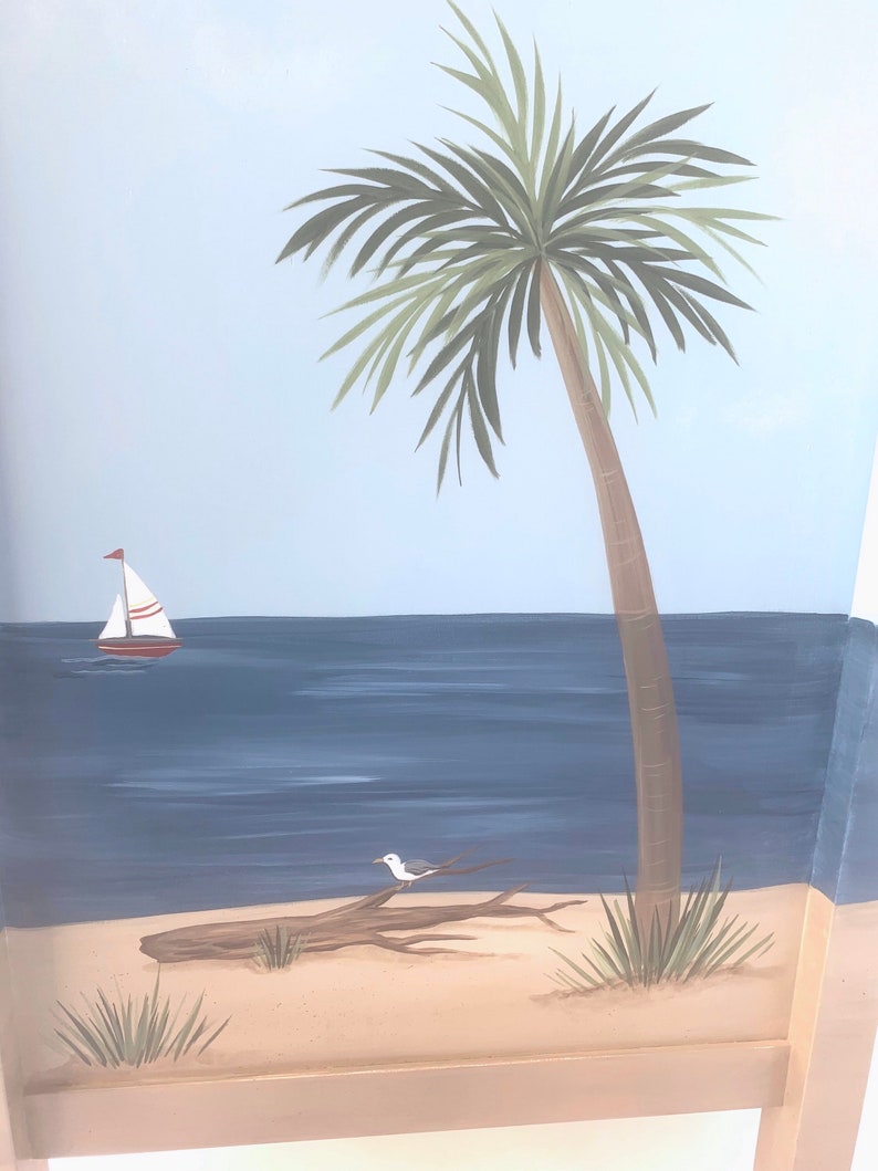 May include: A hand-painted mural depicting a tropical beach scene with a palm tree, a sailboat, a seagull perched on a driftwood log, and blue water. The mural is painted on a light blue background.