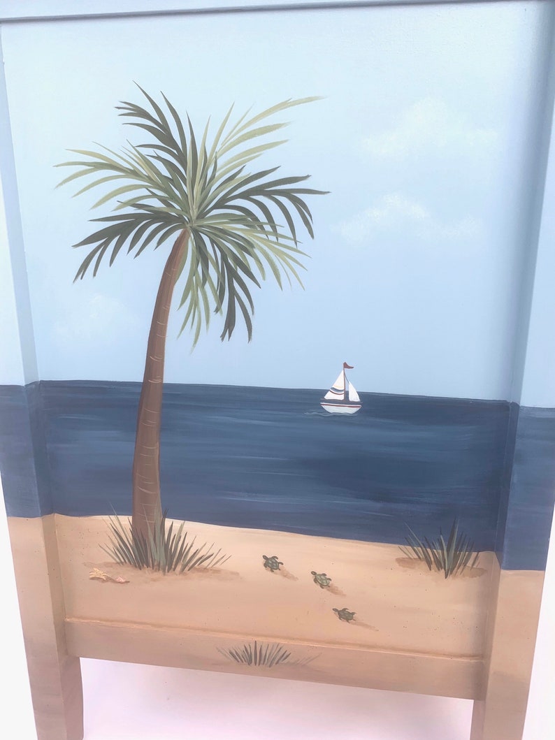May include: A hand-painted wooden panel depicting a beach scene. The panel features a palm tree, a sailboat on the ocean, and sea turtles on the sand.