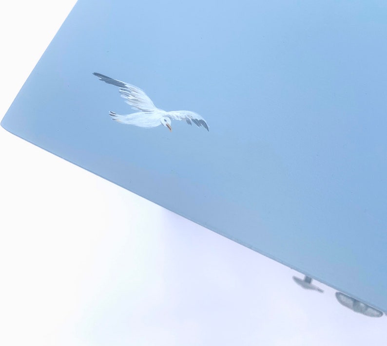 May include: A light blue painted surface with a white seagull flying in the sky.