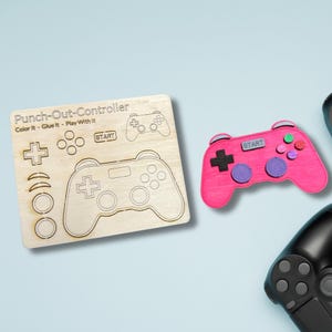 May include: A wooden craft kit for making a video game controller. The kit includes a pre-cut wooden board with the outline of a controller, along with separate pieces for the buttons and joysticks. The text "Punch-Out-Controller" is printed on the board, along with the instructions "Color It - Glue It - Play With It".